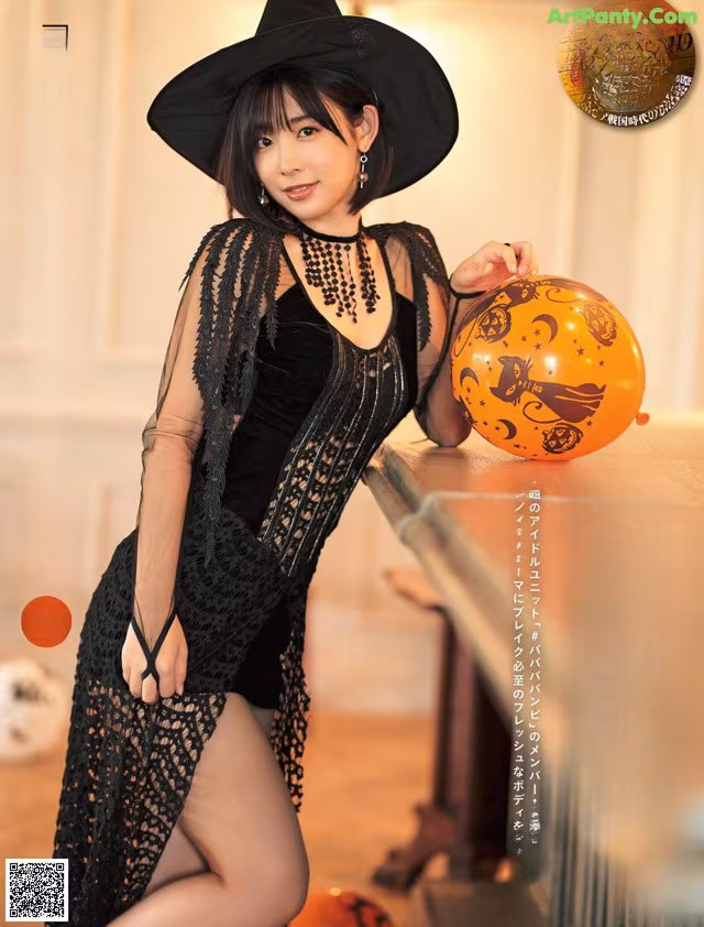 A woman in a black dress and hat holding a pumpkin.