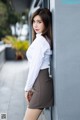 A woman in a white shirt and brown skirt leaning against a wall.