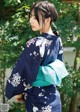 A woman wearing a blue and white kimono standing in front of a tree.