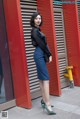 A woman in a black shirt and blue skirt standing in front of a red wall.