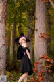 A woman in a black dress and purple hat standing in the woods.